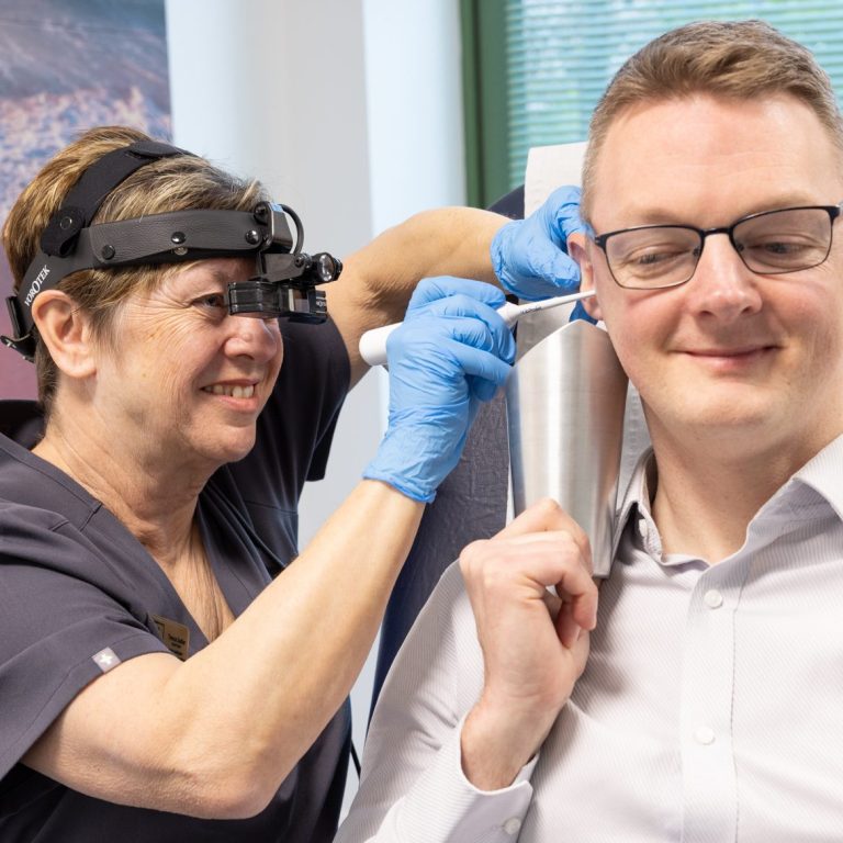 Female Audiologist wearing specialist head loupes whilst carrying out ear irrigation on a patient