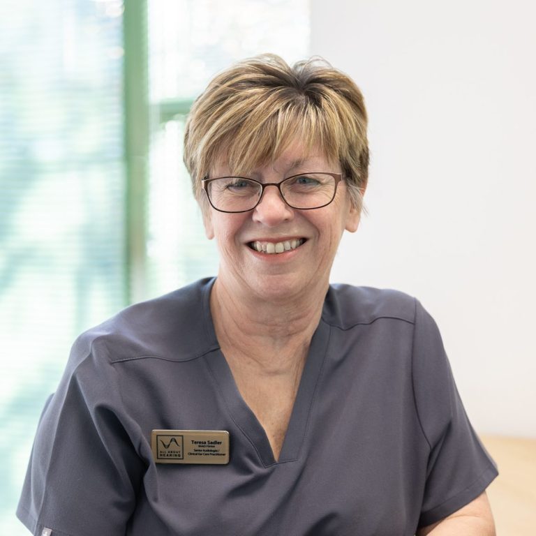 All About Hearing Audiologist, Teresa Sadler, smiling at her desk