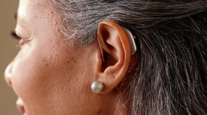 Female wearing a silver Widex Allure RIC hearing aid on her left ear