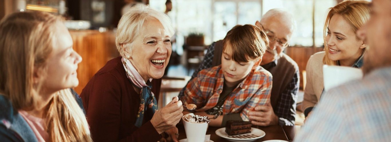 A multi-generational family enjoying coffee and cake, whilst laughing at a coffee shop.
