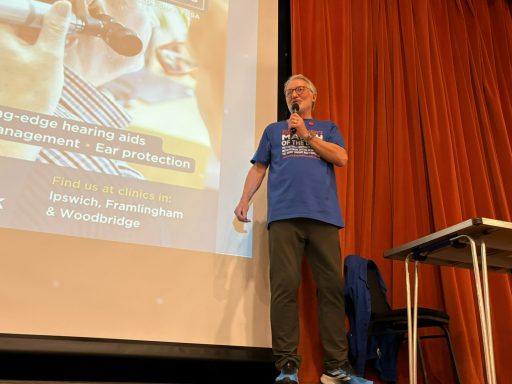 ITFC legend Russell Osman up on the stage holding a microphone to his lips as he presents the All About Hearing Quiz Night