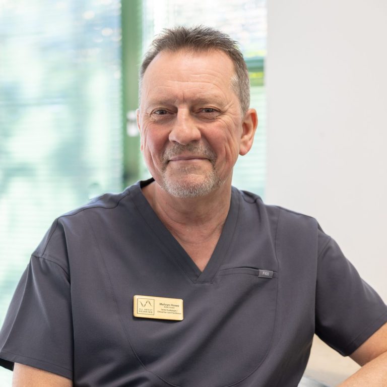 All About Hearing Audiologist, Melvyn Howe, smiling at his desk