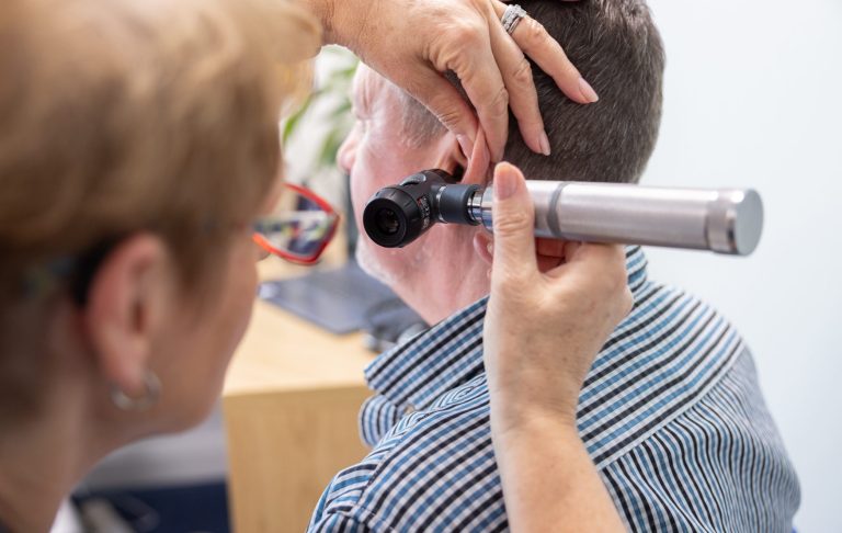 Audiologist performing otoscopy on a male patient using an otoscope