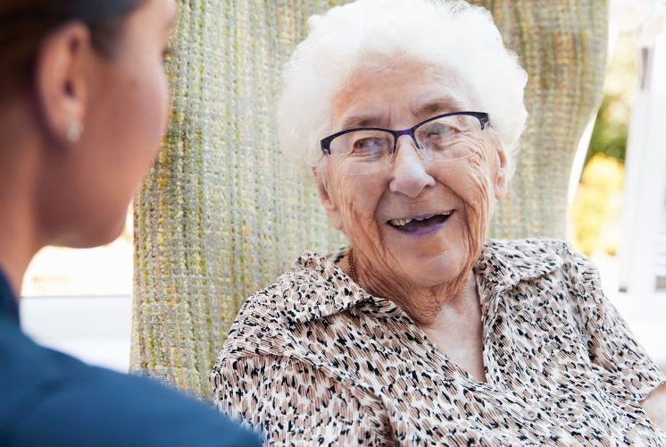 Female Audiologist seeing a female patient at home. Both ladies are smiling.