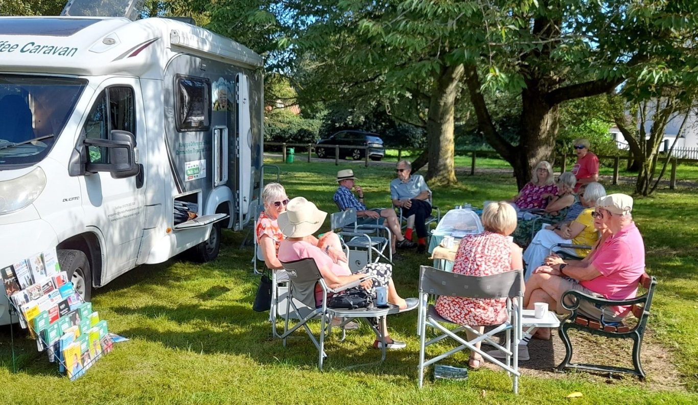 Rural Coffee Caravan holding an outdoor gathering. People sitting on chairs in a circle enjoying coffee