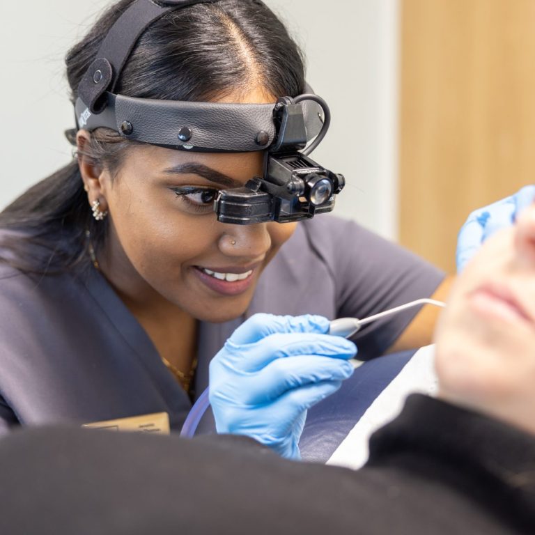 Female Audiologist wearing specialist head loupe whilst conducting microsuction earwax removal on a female patient who is lying down.