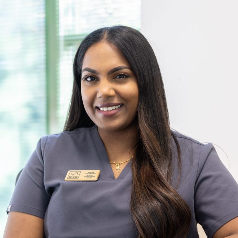 All About Hearing Audiologist, Jenette Jojo-Thomas, smiling at her desk